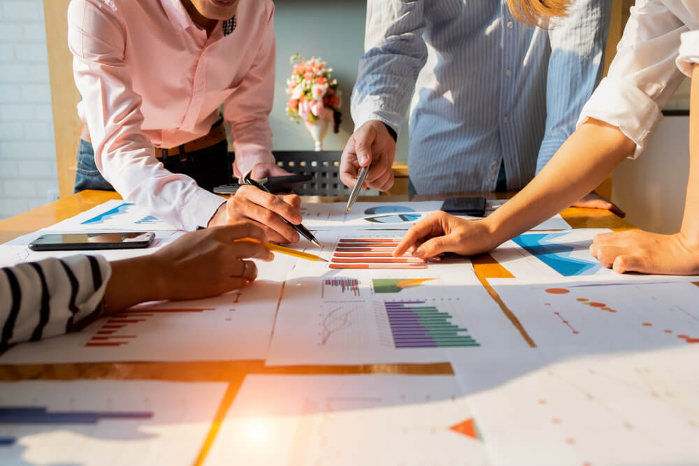 Empresários analisando relatórios financeiros e gráficos sobre uma mesa, representando planejamento contábil e checklist empresarial.