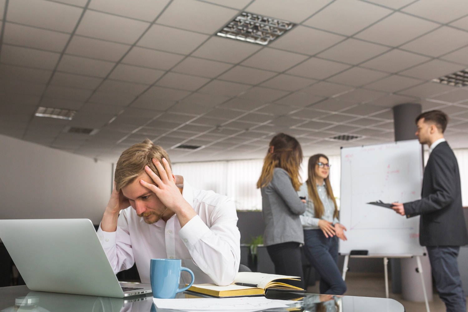 Empresário preocupado no escritório enquanto equipe discute problemas trabalhistas ao fundo, representando erros na gestão trabalhista.