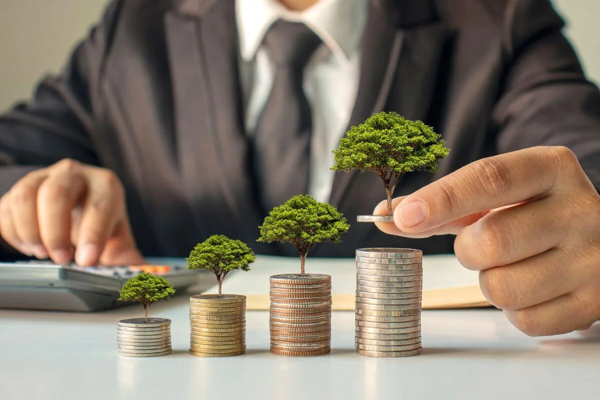 Empresário analisando crescimento financeiro com pilhas de moedas e árvores simbolizando planejamento e gestão financeira empresarial.